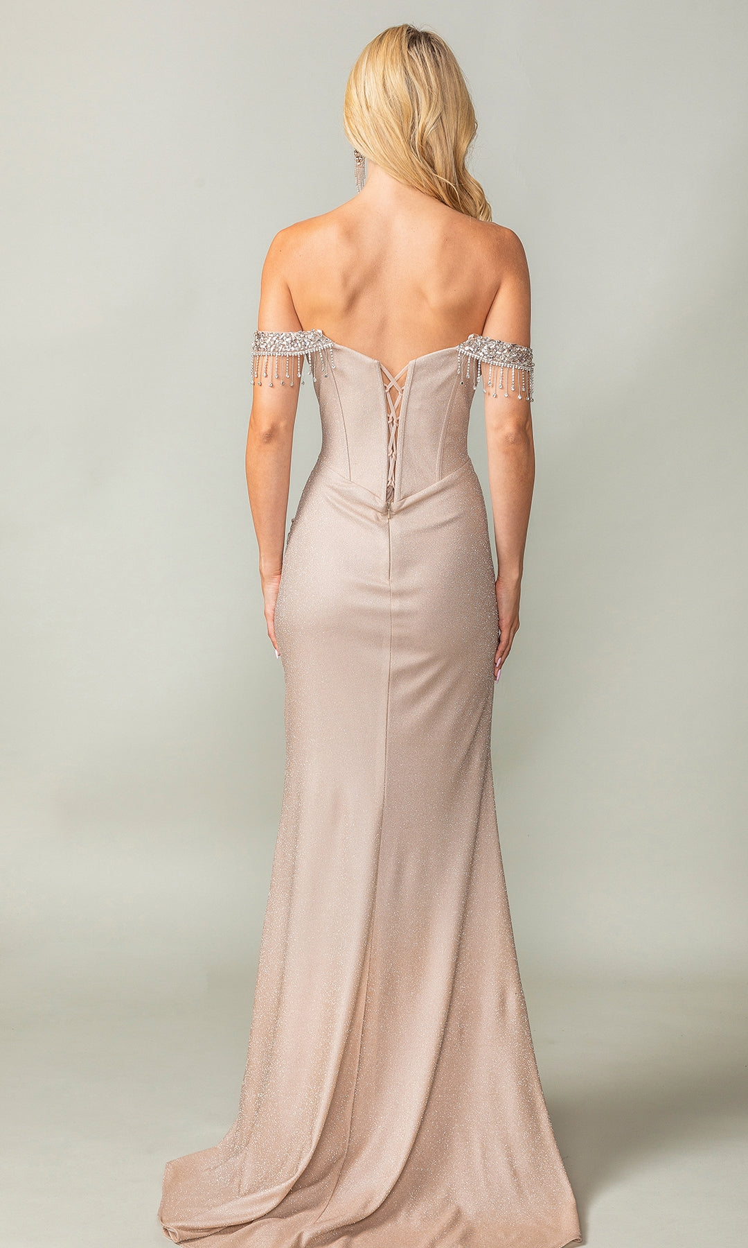 A woman with long blonde hair wears the Dancing Queen 4368 Fringe Long Glitter Prom Dress in light gold, featuring a lace-up back, beaded sleeves, and a form-fitting silhouette, standing against a plain background.